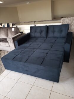Blue tufted sectional sofa bed in an open chaise configuration on a showroom floor.